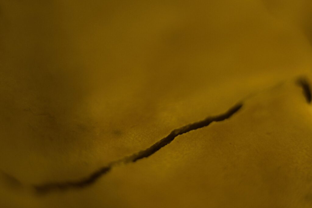 Abstrakte Nahaufnahme einer ockerfarbenen Oberfläche mit einer horizontal verlaufenden, sanft geschwungenen Bruchlinie und weichem Lichtspiel.