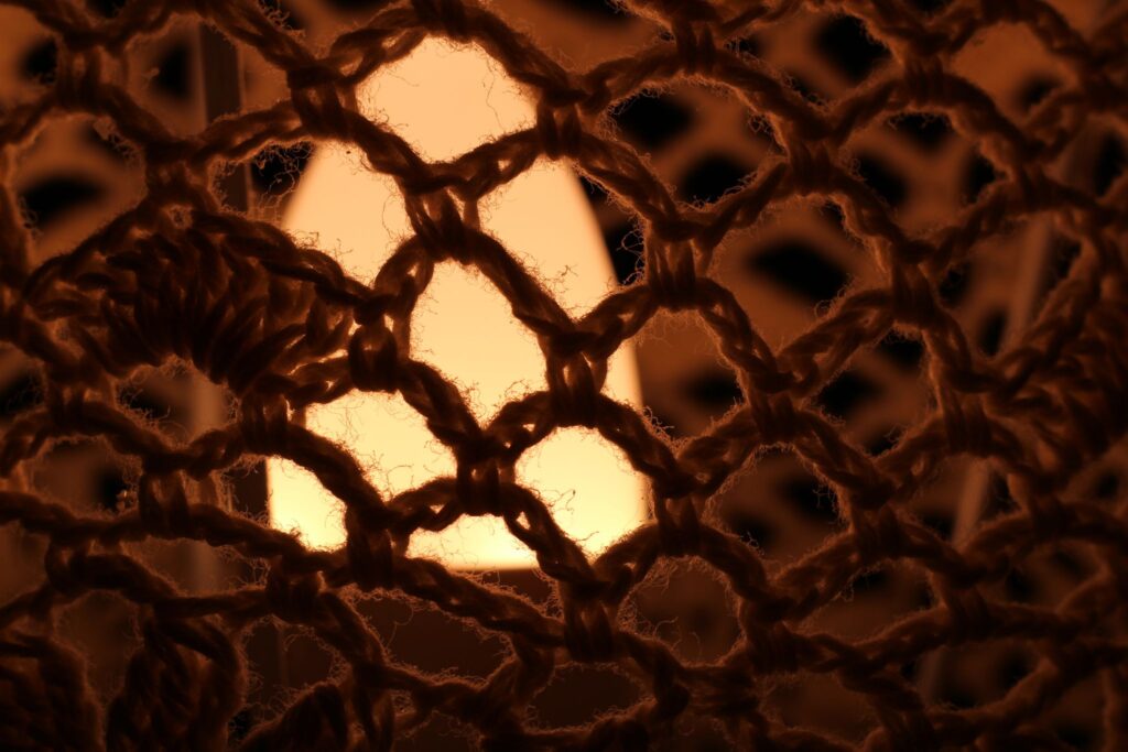 Abstrakte Makrofotografie eines dunklen Textilgewebes vor gelben Licht; künstlerische Detailaufnahme von Häkelstrukturen und feinen Fasern.