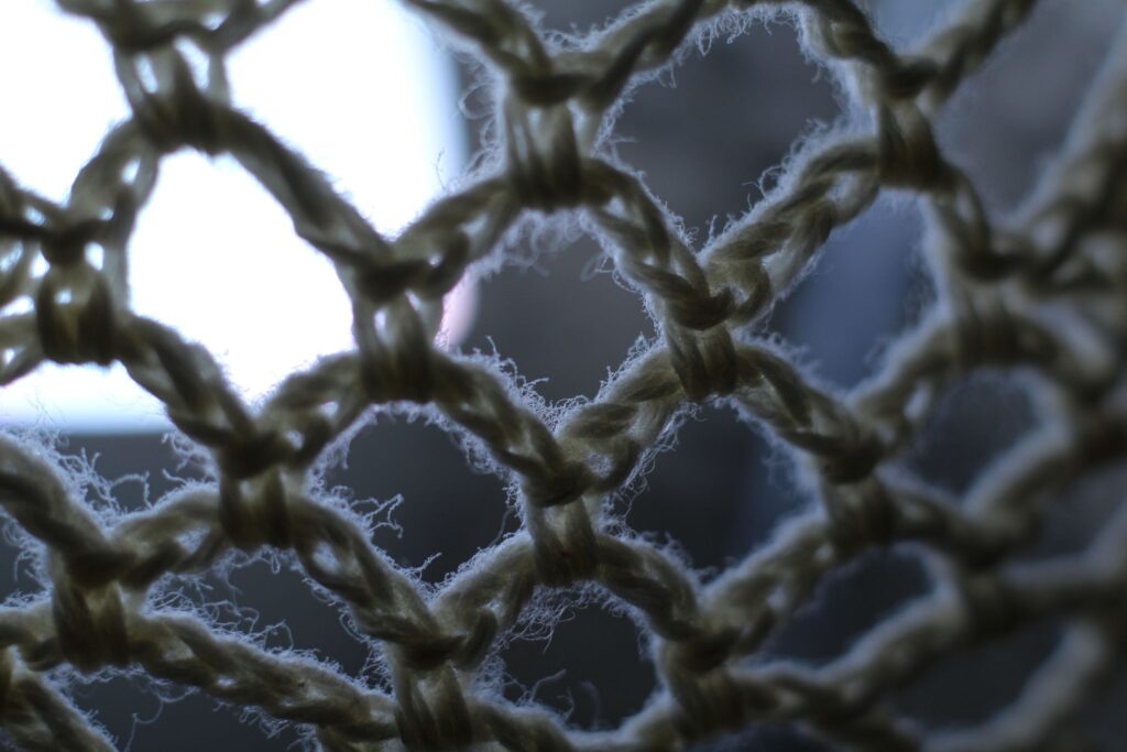 Abstrakte Makrofotografie eines hellen Textilgeflechts vor kühlem Tageslicht; künstlerische Detailaufnahme von groben Garnstrukturen und Fasern mit sanftem Bokeh.