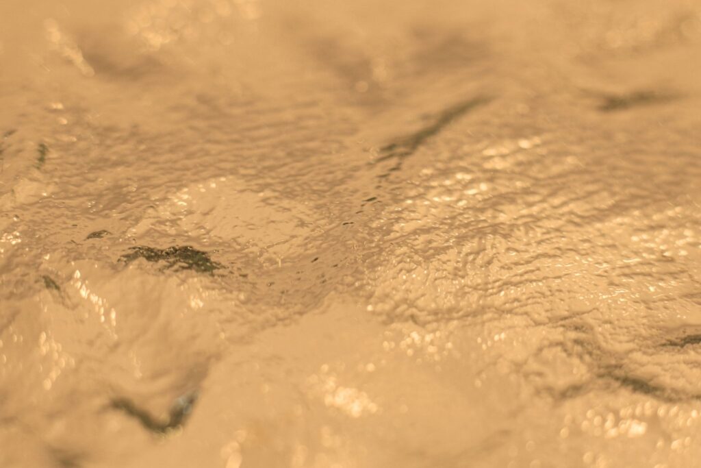 Abstrakte Wasser-Nahaufnahme in Goldtönen mit Lichtreflexionen.
